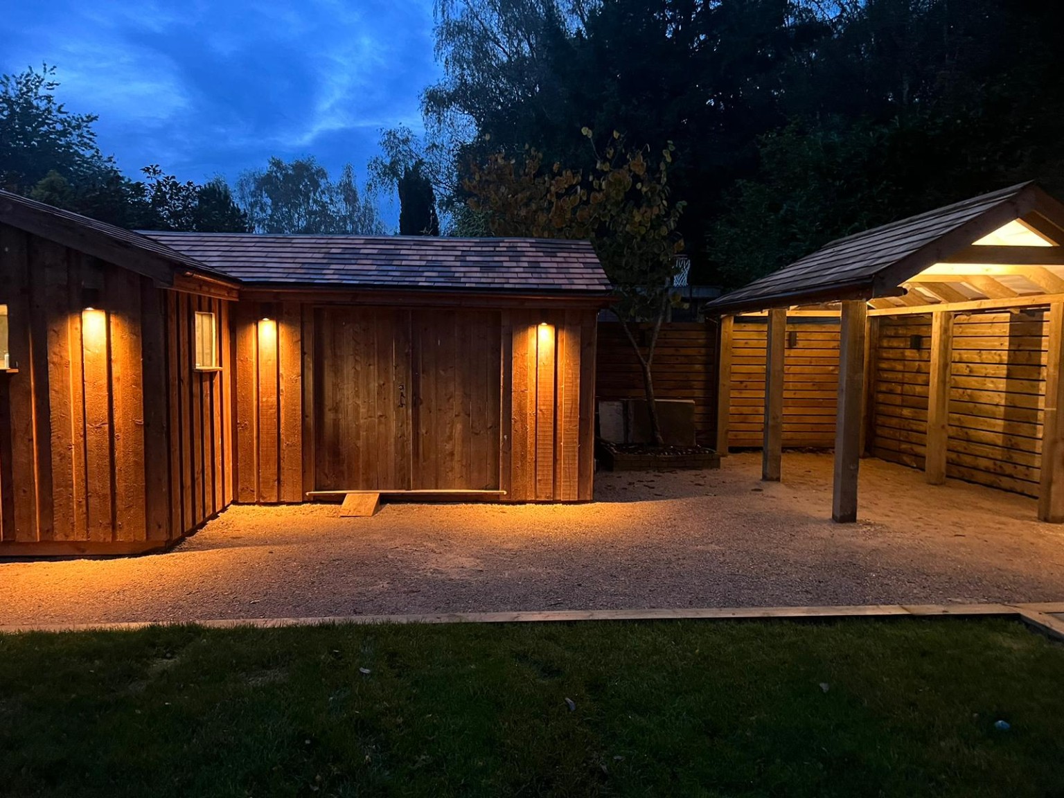 Timber garden room and adjoining shelter illuminated at dusk
