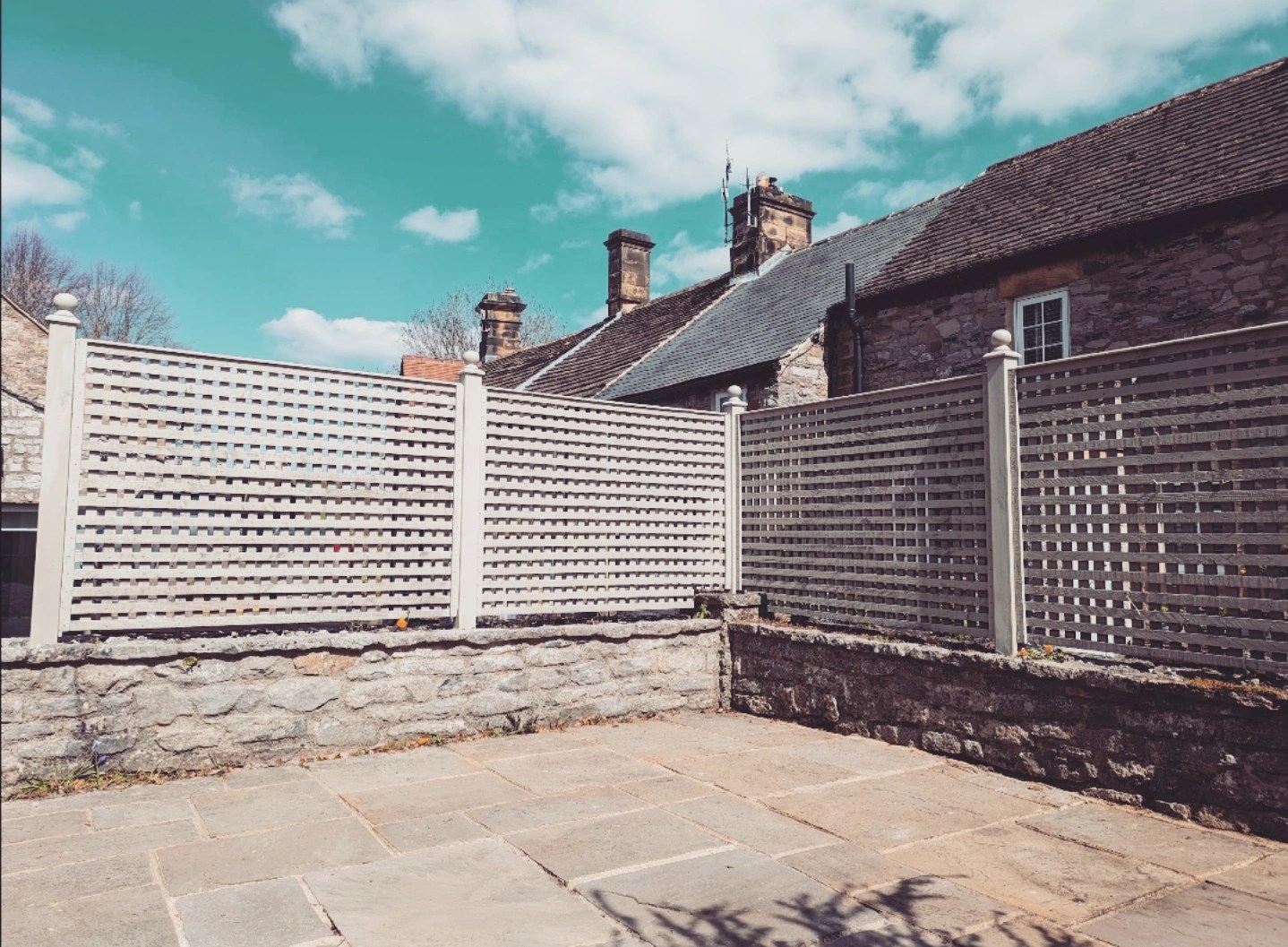 Decorative timber trellis fencing with capped posts above a stone garden wall